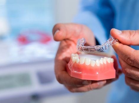 Closeup of woman smiling while holding clear aligner