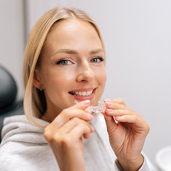 Smiling patient in white shirt holding clear aligner